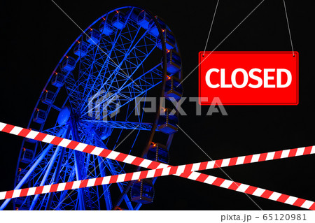 Closed due to a pandemic. Passage to ferris wheel is blocked by red and white ribbon and sign hanging is closed. 65120981