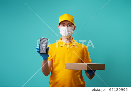Courier with medical mask on his face holds box and smartphone in his hand. Courier with medical mask on his face holds box and smartphone in his hand. 65120996