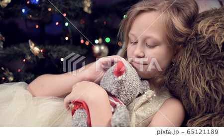 Little lonely girl in a festive dress hugs a rat soft toy while spending time in solitude and self-isolation during a virus pandemic 65121189