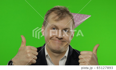 Drunk sleepy young businessman with hangover in festive cap giving thumbs up Drunk sleepy young businessman with hangover in festive cap giving thumbs up 65127893