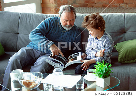 Grandfather and his grandson spending time insulated at home, having fun, reading magazine together, happy 65128892