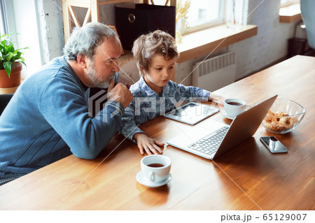 Grandfather and his grandson spending time insulated at home, stadying, watching cinema, shopping together Grandfather and his grandson spending time insulated at home, stadying, watching cinema, shopping together 65129007