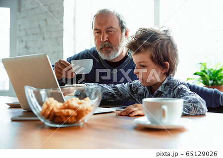 Grandfather and his grandson spending time insulated at home, stadying, watching cinema, shopping together Grandfather and his grandson spending time insulated at home, stadying, watching cinema, shopping together 65129026