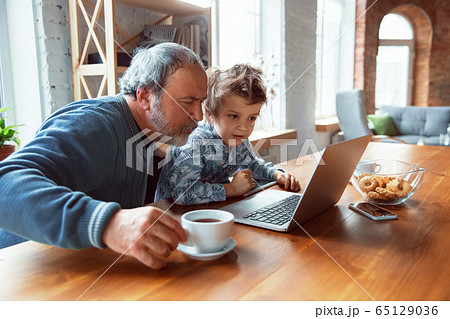 Grandfather and his grandson spending time insulated at home, stadying, watching cinema, shopping together 65129036