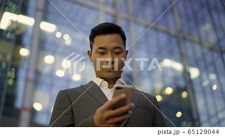 Low angle view of a young asian businessman, leading correspondence on the phone. Downtown district. 65129044