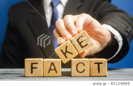 A man puts wooden blocks with the words Fact and fake. Concept of news and false information. Yellow press. 65129969