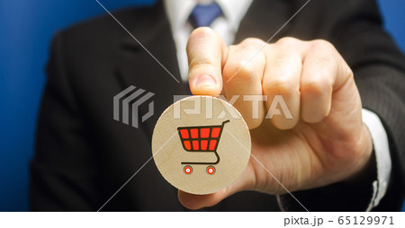 Businessman holds a wooden block with the image of a supermarket cart - shopping trolley. Retail and shopping. Ecommerce and delivery service concept. Marketing. Trade. Sale of products 65129971