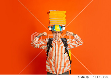 Contacless delivery service during quarantine. Man delivers food and shopping bags during insulation. Emotions of deliveryman isolated on orange background. Contacless delivery service during quarantine. Man delivers food and shopping bags during insulation. Emotions of deliveryman isolated on orange background. 65130490