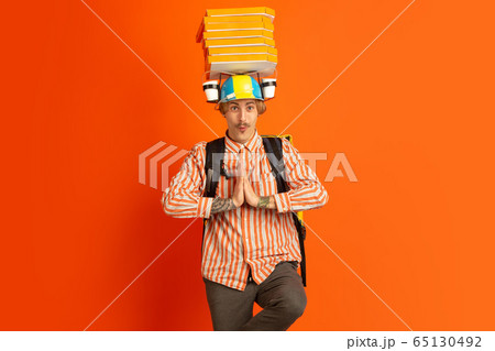 Contacless delivery service during quarantine. Man delivers food and shopping bags during insulation. Emotions of deliveryman isolated on orange background. Contacless delivery service during quarantine. Man delivers food and shopping bags during insulation. Emotions of deliveryman isolated on orange background. 65130492