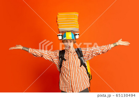 Contacless delivery service during quarantine. Man delivers food and shopping bags during insulation. Emotions of deliveryman isolated on orange background. 65130494