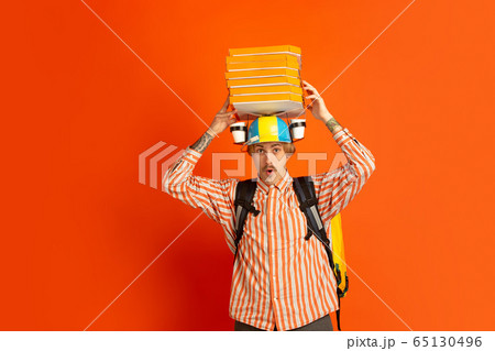 Contacless delivery service during quarantine. Man delivers food and shopping bags during insulation. Emotions of deliveryman isolated on orange background. Contacless delivery service during quarantine. Man delivers food and shopping bags during insulation. Emotions of deliveryman isolated on orange background. 65130496