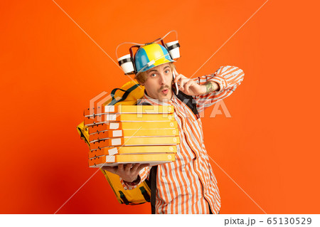 Contacless delivery service during quarantine. Man delivers food and shopping bags during insulation. Emotions of deliveryman isolated on orange background. Contacless delivery service during quarantine. Man delivers food and shopping bags during insulation. Emotions of deliveryman isolated on orange background. 65130529