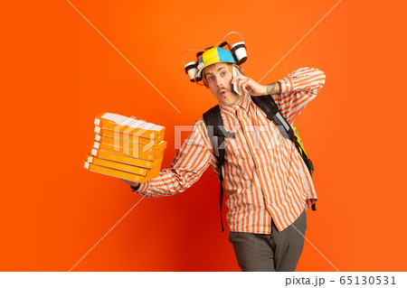 Contacless delivery service during quarantine. Man delivers food and shopping bags during insulation. Emotions of deliveryman isolated on orange background. 65130531