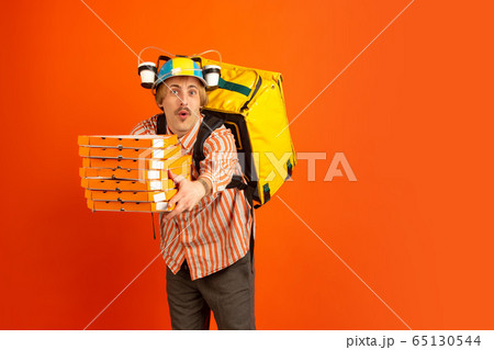 Contacless delivery service during quarantine. Man delivers food and shopping bags during insulation. Emotions of deliveryman isolated on orange background. 65130544