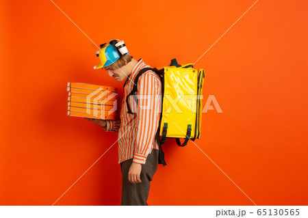 Contacless delivery service during quarantine. Man delivers food and shopping bags during insulation. Emotions of deliveryman isolated on orange background. 65130565