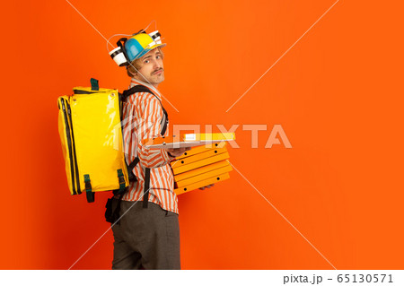 Contacless delivery service during quarantine. Man delivers food and shopping bags during insulation. Emotions of deliveryman isolated on orange background. 65130571