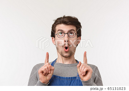 Close-up portrait of interested and excited caucasian bearded guy in apron and glasses, say wow and stare pointing fingers up at something cool, spot awesome product, white background Close-up portrait of interested and excited caucasian bearded guy in apron and glasses, say wow and stare pointing fingers up at something cool, spot awesome product, white background 65131023