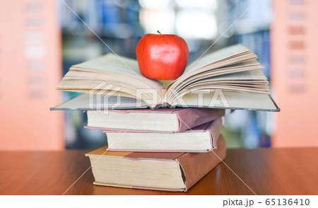 An apple on the books on the table with bookshelf An apple on the books on the table with bookshelf 65136410