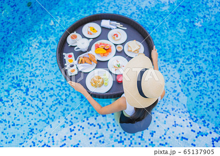 Portrait beautiful young asian woman happy smile with floating breakfast in tray on swimming pool 65137905