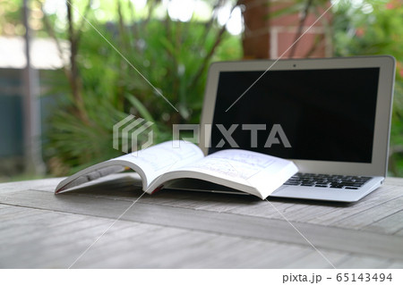 Open book on top of computer laptop. Garden view. 65143494