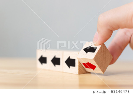 Hand flip over wooden cube block with red arrow facing the opposite direction black arrows 65146473