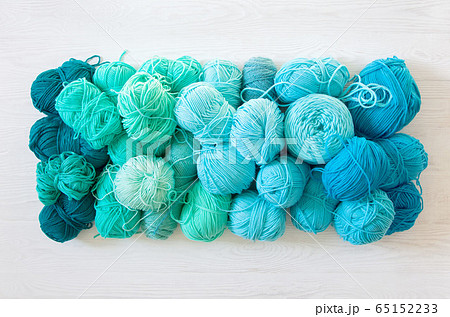 Yarn of green, turquoise, aquamarine and blue colors. White wood background. Knitting needles and crochet hooks. Scissors. White background. Yarn of green, turquoise, aquamarine and blue colors. White wood background. Knitting needles and crochet hooks. Scissors. White background. 65152233