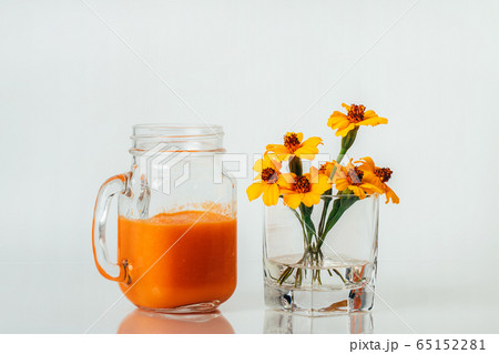 Orange and carrot smoothie in glass jar and glass with flowers on white background Orange and carrot smoothie in glass jar and glass with flowers on white background 65152281
