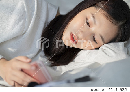 ベッドに寝転ぶ若い女性 65154926