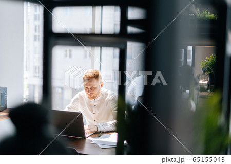 Attractive young business man typing on laptop doing research against window. Attractive young business man typing on laptop doing research against window. 65155043