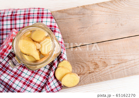 Opened glass jar with ginger water on red tartan cloth on diagonal wooden boards. Trendy healthy detox isotonic drink. Natural infusion for normalization of metabolism and weight. Top view, copy space 65162270