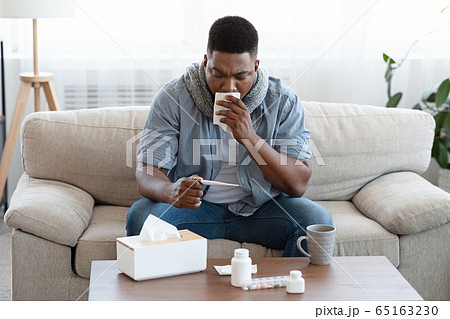 Seasonal Flu. Sick Afro Guy Checking His Body Temperature At Home Seasonal Flu. Sick Afro Guy Checking His Body Temperature At Home 65163230