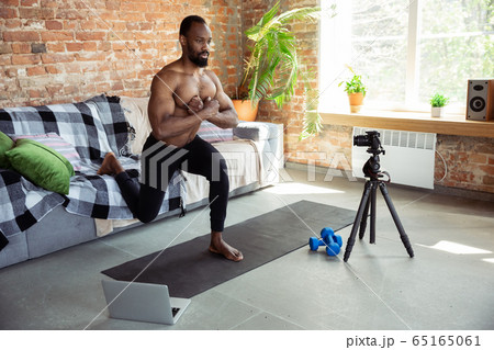 Young african-american man teaching at home online courses of fitness, aerobic, sporty lifestyle during quarantine, reording on camera, streaming Young african-american man teaching at home online courses of fitness, aerobic, sporty lifestyle during quarantine, reording on camera, streaming 65165061