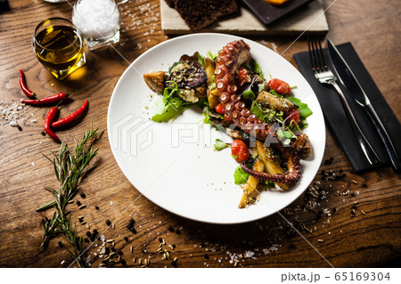 Warm octopus salad with stir fried vegetables and aji sauce on white plate. Delicious healthy mediterranean traditional seafood closeup served on a table for lunch. Warm octopus salad with stir fried vegetables and aji sauce on white plate. Delicious healthy mediterranean traditional seafood closeup served on a table for lunch. 65169304
