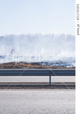 a strong fire, flame and a lot of smoke near the paved highway route, burning dry grass 65170565