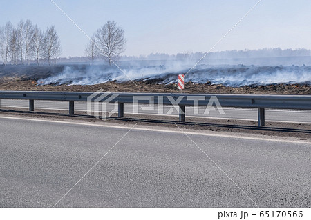 a strong fire, flame and a lot of smoke near the paved highway route, burning dry grass 65170566