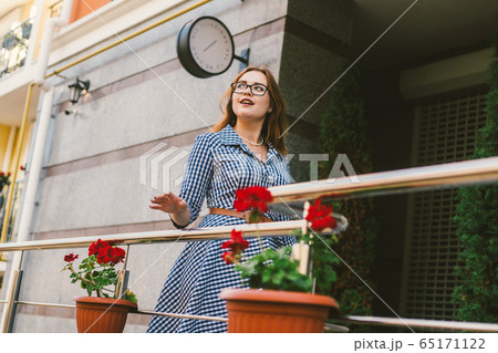 The topic of renting a house in Europe for summer holidays. A young Caucasian woman in a dress poses on a terrace of apartments decorated with flowerpots with plants. Girl near the hotel The topic of renting a house in Europe for summer holidays. A young Caucasian woman in a dress poses on a terrace of apartments decorated with flowerpots with plants. Girl near the hotel 65171122