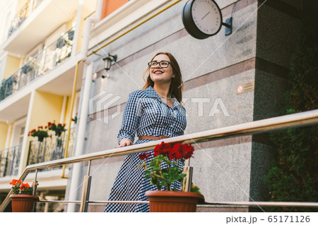 The topic of renting a house in Europe for summer holidays. A young Caucasian woman in a dress poses on a terrace of apartments decorated with flowerpots with plants. Girl near the hotel The topic of renting a house in Europe for summer holidays. A young Caucasian woman in a dress poses on a terrace of apartments decorated with flowerpots with plants. Girl near the hotel 65171126