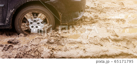 The car got stuck on a dirt road in the mud. Wheel of a car stuck in the mud on the road. Car on a The car got stuck on a dirt road in the mud. Wheel of a car stuck in the mud on the road. Car on a 65171795