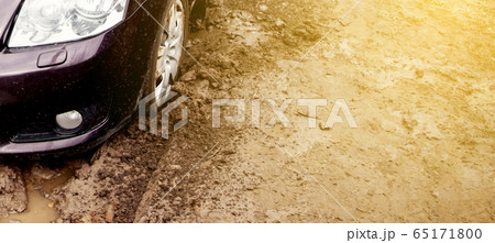 The car got stuck on a dirt road in the mud. Wheel of a car stuck in the mud on the road. Car on a 65171800