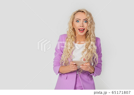 Surprised, excited, beautiful blonde curly woman playing a game for a smartphone, holding a mobile Surprised, excited, beautiful blonde curly woman playing a game for a smartphone, holding a mobile 65171807