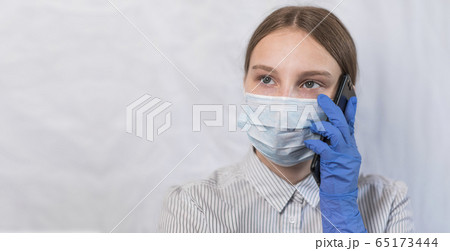 teenager girl of 12-15 years old, in protective medical mask, calls on her smartphone, listens to her parent's voice message, quarantine hospital and self-isolation home in medical chamber. teenager girl of 12-15 years old, in protective medical mask, calls on her smartphone, listens to her parent's voice message, quarantine hospital and self-isolation home in medical chamber. 65173444