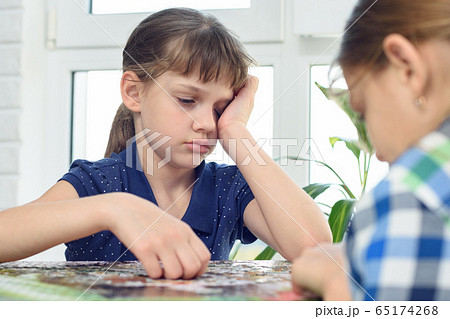 Tired girl reluctantly collects jigsaw puzzles 65174268