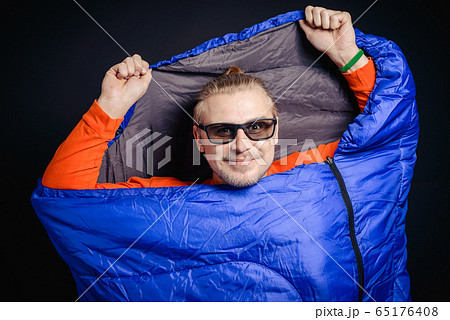 A young guy in sunglasses posing in a sleeping bag 65176408