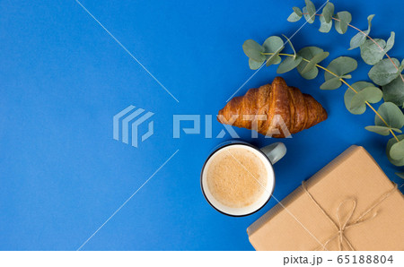 Present box, coffee, croissant and eucalyptus leaves on Blue background. Good Morning, holiday concept. Flat lay banner, top view, Sustainable lifestyle. Composition for birthday, mother day or xmas Present box, coffee, croissant and eucalyptus leaves on Blue background. Good Morning, holiday concept. Flat lay banner, top view, Sustainable lifestyle. Composition for birthday, mother day or xmas 65188804