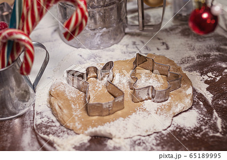 raw gingerbread brown spicy dough with metal shapes of angel and christmas tree on a wooden table with caramel cane and red christmas toys 65189995