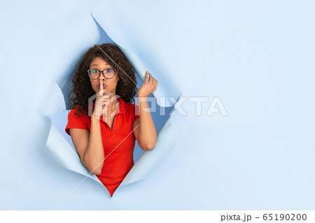 Cheerful young woman poses in torn blue paper hole background, emotional and expressive 65190200