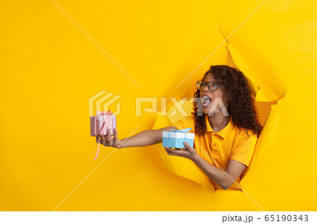 Cheerful young woman poses in torn yellow paper hole background, emotional and expressive 65190343