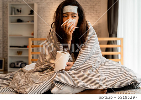 Young Asian woman suffering from cold and illness and lying in bed with tissue at home 65195297