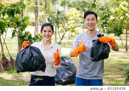 Young Asian male and female couple volunteers with gloves giving thumbs up while collecting garbage waste into trash bag in green park Young Asian male and female couple volunteers with gloves giving thumbs up while collecting garbage waste into trash bag in green park 65195456
