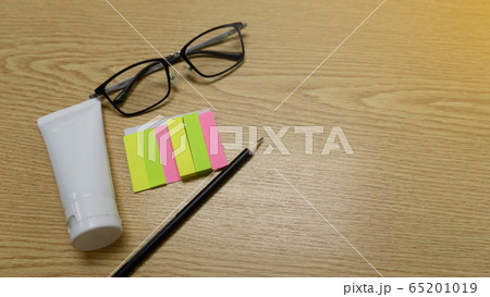 Top view of black pencil, eyeglassese and colorful paper postit on workspce brown wooden table. Top view of black pencil, eyeglassese and colorful paper postit on workspce brown wooden table. 65201019